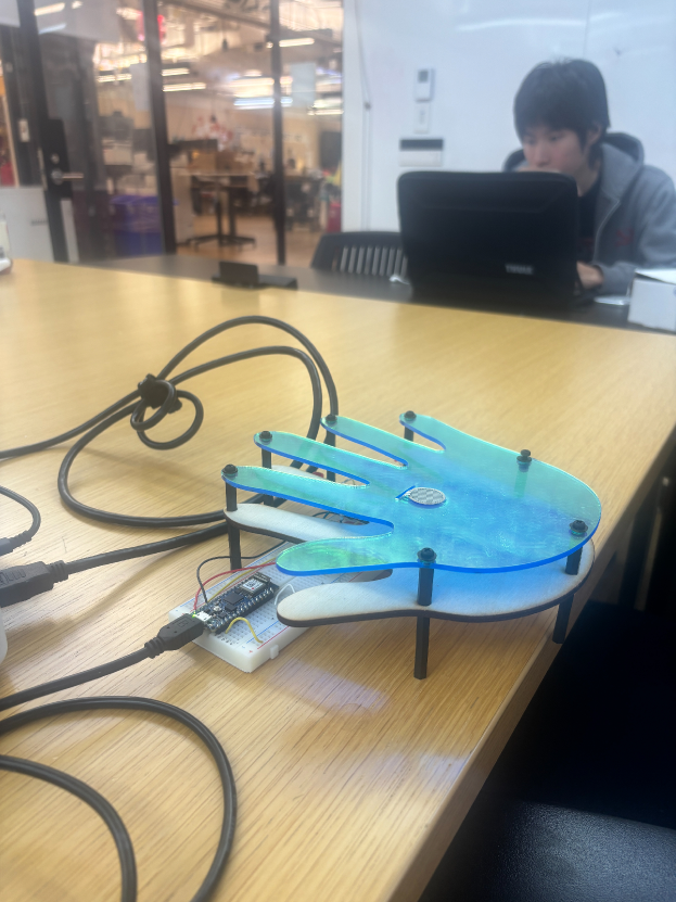 Trance: acrylic hand sculpture with layered blue-green panels, Arduino breadboard and pressure sensor visible underneath, on a wooden desk